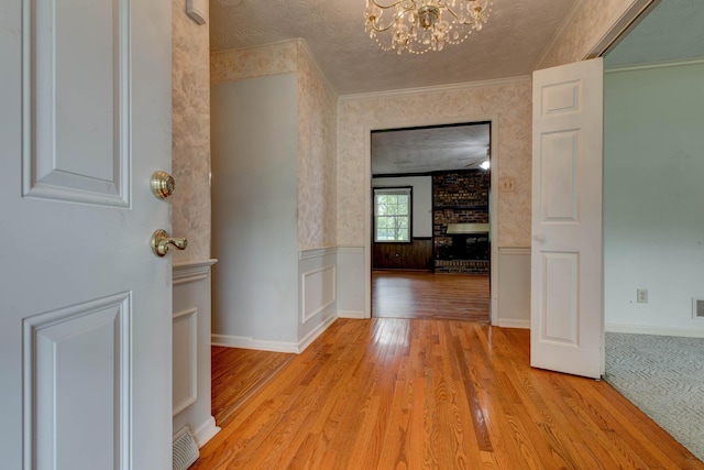 230 Fairway Dr, Nicholasville, KY 40356 - hallway with light wood finished floors, a wainscoted wall, a textured ceiling, a chandelier, and crown molding