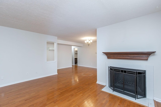 421 Redding Rd Unit 99, Lexington, KY 40517 - unfurnished living room with a chandelier, wood finished floors, a tiled fireplace, and a textured ceiling