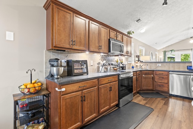 821 White Wood Flt, Lexington, KY 40511 - kitchen featuring appliances with stainless steel finishes, dark wood-style flooring, vaulted ceiling, brown cabinets, and backsplash