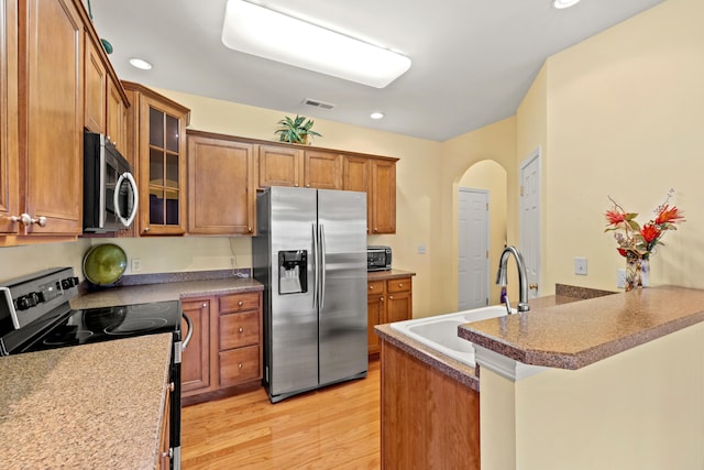 139 Delissa Dr, Georgetown, KY 40324 - kitchen featuring appliances with stainless steel finishes, a peninsula, brown cabinetry, light wood-type flooring, and glass insert cabinets