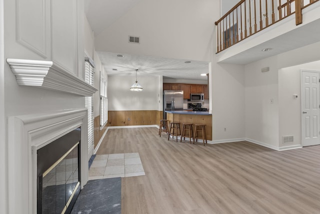 1048 Vero Ct, Lexington, KY 40509 - living room featuring light wood-style flooring, a fireplace with flush hearth, wainscoting, a towering ceiling, and wooden walls