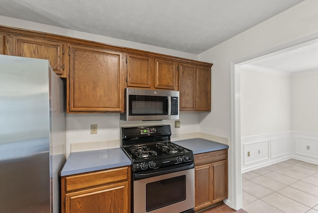 1048 Vero Ct, Lexington, KY 40509 - kitchen with appliances with stainless steel finishes, brown cabinets, wainscoting, light tile patterned floors, and crown molding