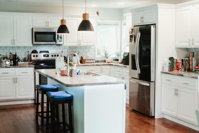 585 Cotton Rd, Corbin, KY 40701 - kitchen featuring appliances with stainless steel finishes, dark wood-type flooring, tasteful backsplash, a kitchen bar, and white cabinetry