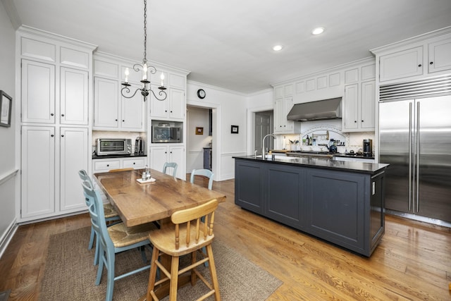 321 S Turner St, Midway, KY 40347 - kitchen featuring built in appliances, dark countertops, wall chimney exhaust hood, white cabinetry, and backsplash