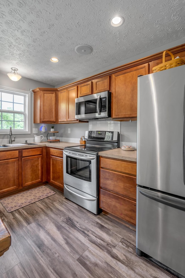 1701 Keating Dr, Louisville, KY 40245 - kitchen with appliances with stainless steel finishes, wood finished floors, brown cabinets, light countertops, and a textured ceiling