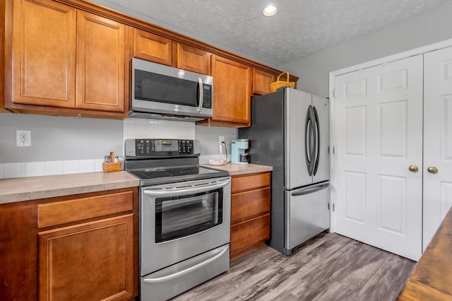 1701 Keating Dr, Louisville, KY 40245 - kitchen with stainless steel appliances, brown cabinetry, wood finished floors, a textured ceiling, and light countertops