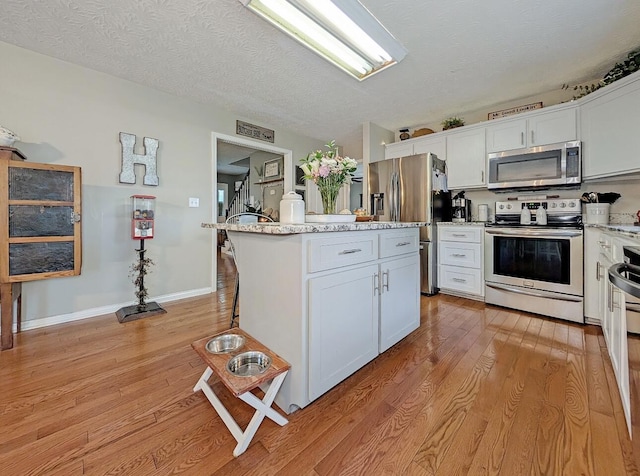 109 Edwards Ct, Lancaster, KY 40444 - kitchen featuring appliances with stainless steel finishes, light wood finished floors, white cabinetry, a kitchen island, and a textured ceiling