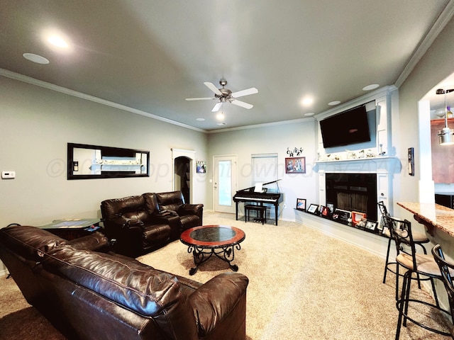 living area featuring crown molding, carpet, a fireplace with raised hearth, and a ceiling fan