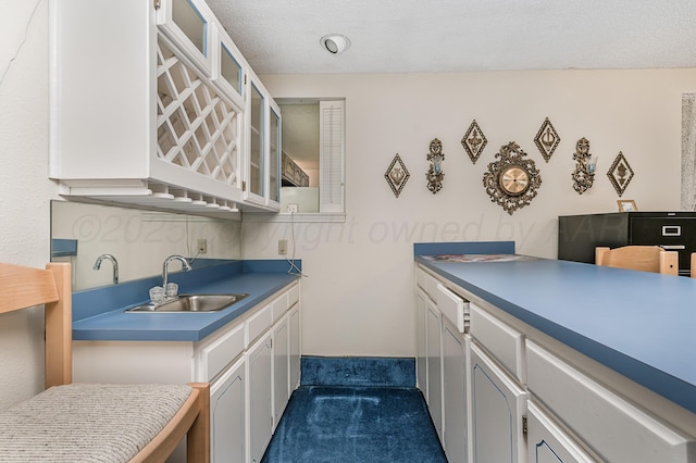 kitchen with white cabinets, glass insert cabinets, a sink, and dark carpet