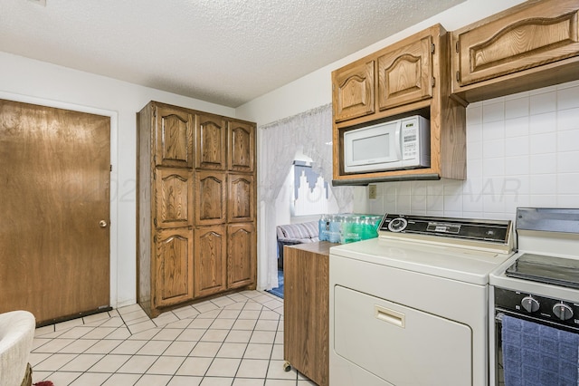 clothes washing area with a textured ceiling, laundry area, light tile patterned flooring, and washing machine and clothes dryer