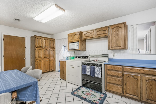kitchen featuring brown cabinetry, a textured ceiling, visible vents, electric stove, and washer / dryer