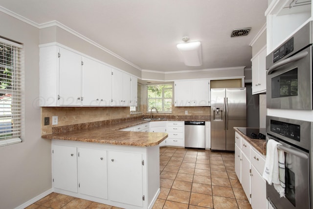 3203 S Austin St, Amarillo, TX 79109 - kitchen featuring appliances with stainless steel finishes, a peninsula, backsplash, white cabinetry, and ornamental molding