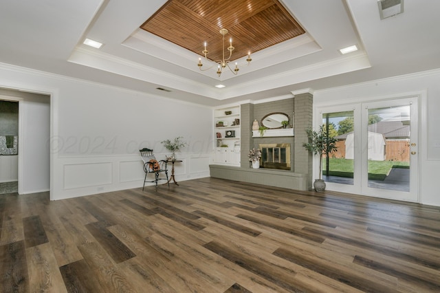 unfurnished living room featuring built in shelves, dark hardwood / wood-style floors, a fireplace, a raised ceiling, and crown molding