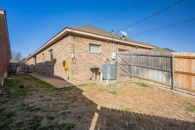 rear view of house featuring a gate, a fenced backyard, brick siding, and central AC