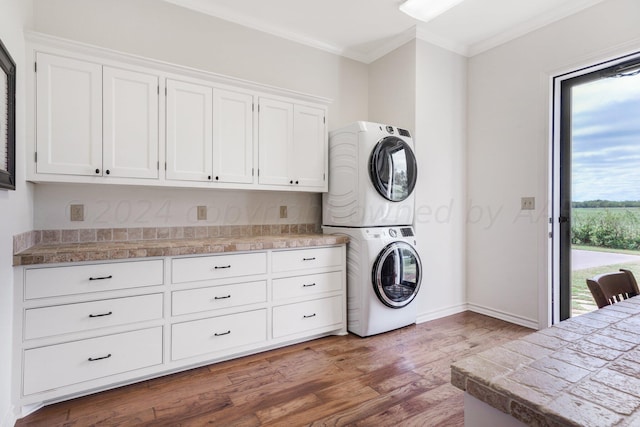 clothes washing area with cabinets, stacked washer and clothes dryer, crown molding, and wood-type flooring