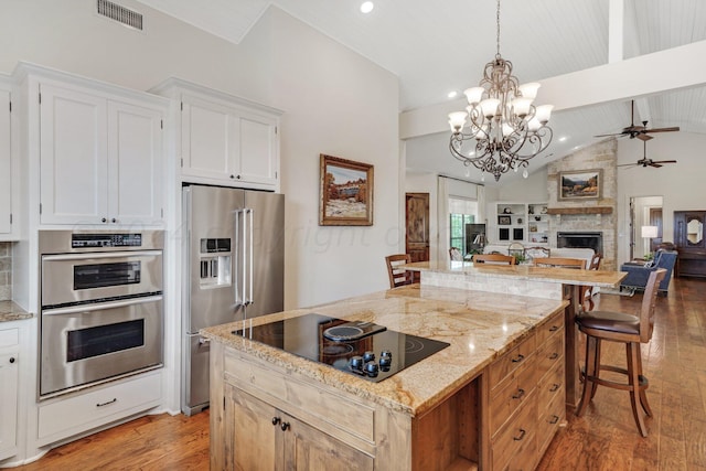 kitchen with vaulted ceiling with beams, a center island, stainless steel appliances, white cabinetry, and light hardwood / wood-style flooring