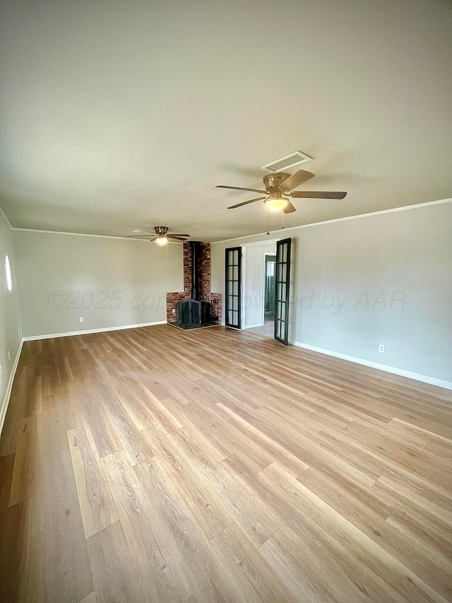 unfurnished living room with a wood stove, light wood-style floors, and baseboards