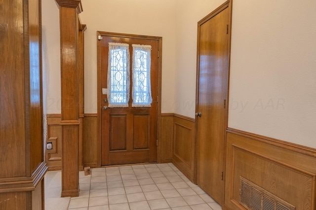 doorway with wood walls, light tile patterned floors, and ornate columns