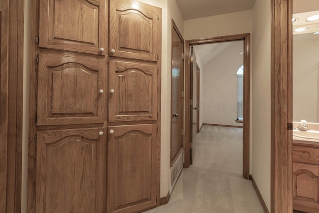 hall with sink, vaulted ceiling, and light carpet