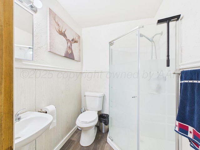 full bath with toilet, a wainscoted wall, a sink, a stall shower, and wood finished floors