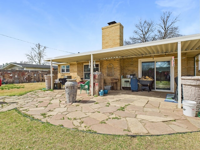 rear view of property featuring fence, a chimney, a patio, and brick siding