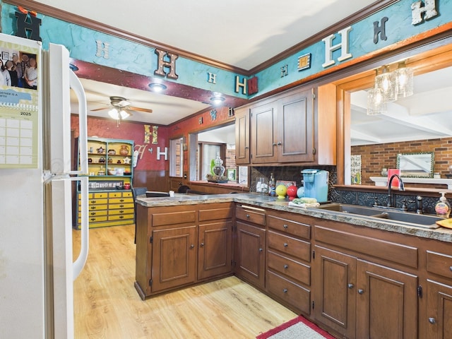 kitchen with a sink, light wood finished floors, freestanding refrigerator, a ceiling fan, and a peninsula
