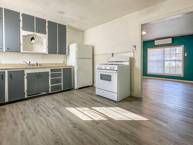 kitchen with light hardwood / wood-style floors, a wall mounted AC, a textured ceiling, white appliances, and gray cabinets