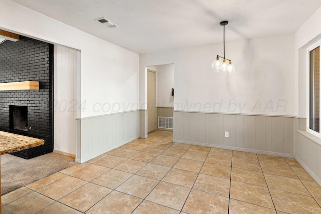 tiled spare room featuring a chandelier, a textured ceiling, and a brick fireplace