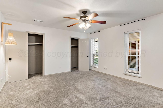 unfurnished bedroom with carpet, ceiling fan, and two closets