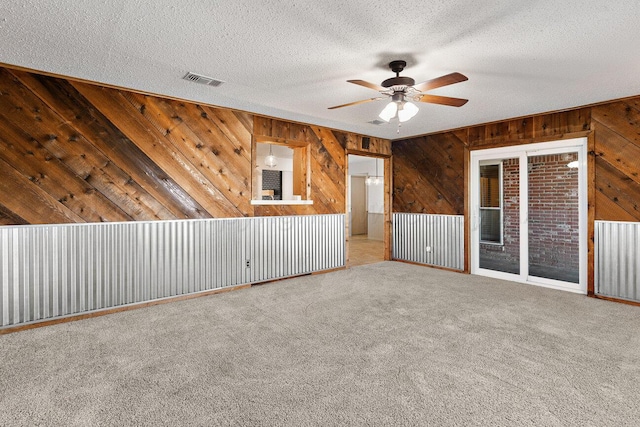 unfurnished room featuring wood walls, carpet floors, a textured ceiling, and ceiling fan