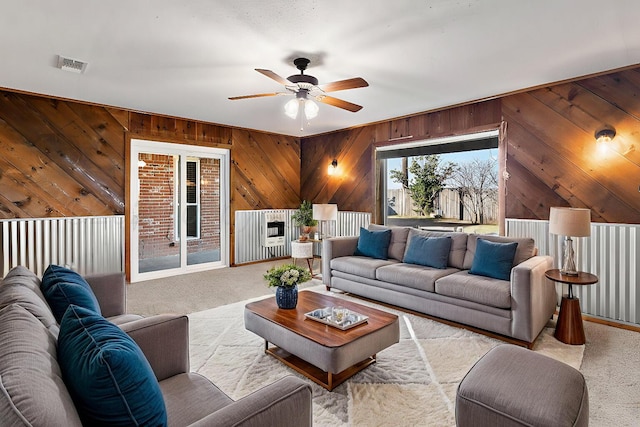 carpeted living room with ceiling fan and wood walls