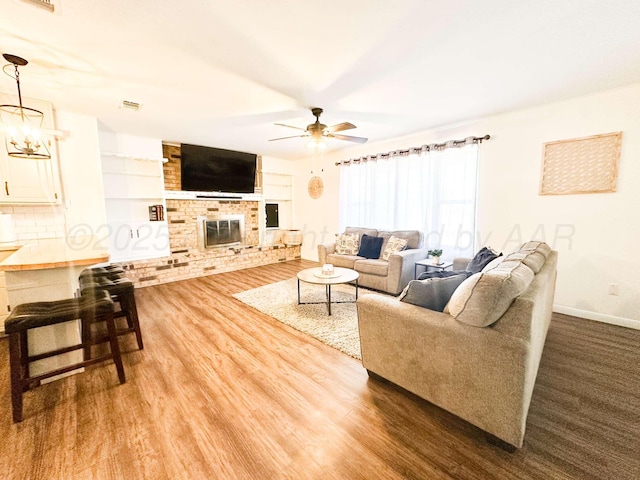 living room with dark wood-style flooring, visible vents, baseboards, a fireplace, and ceiling fan with notable chandelier