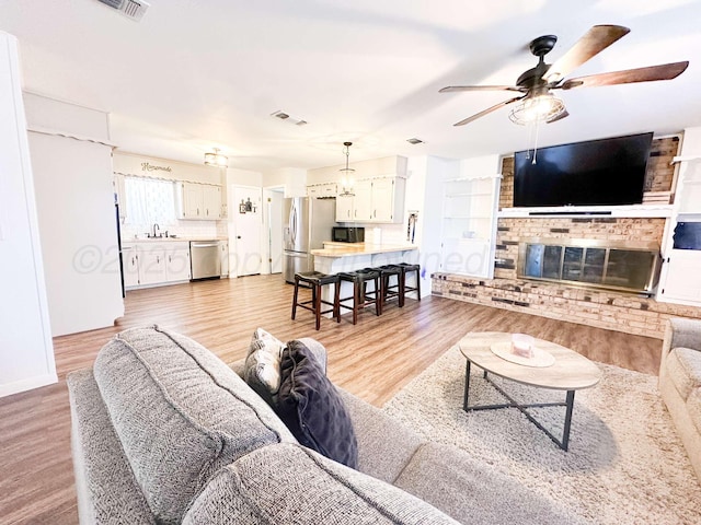 living room featuring a brick fireplace, visible vents, light wood-style floors, and a ceiling fan