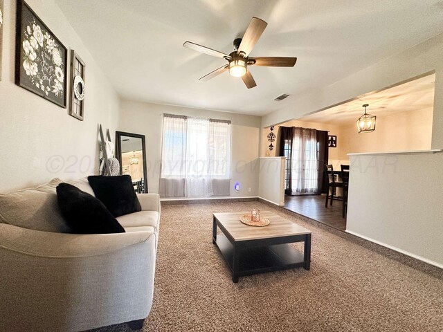 living room featuring ceiling fan with notable chandelier, carpet, baseboards, and visible vents