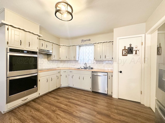 kitchen with light countertops, dark wood-style flooring, under cabinet range hood, a sink, and appliances with stainless steel finishes