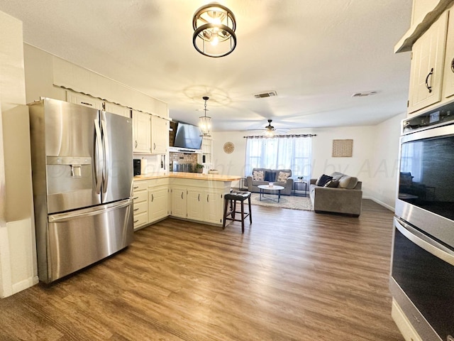 kitchen with dark wood finished floors, visible vents, appliances with stainless steel finishes, and a peninsula