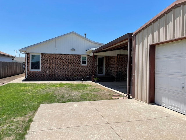 back of property featuring brick siding, a garage, fence, and a lawn