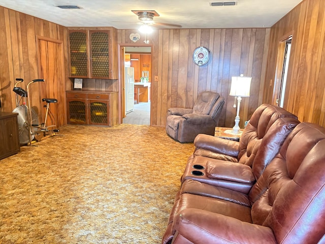 living room featuring carpet, ceiling fan, wooden walls, and visible vents