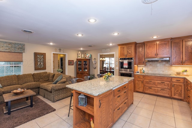 2314 Atkinsen St, Amarillo, TX 79106 - kitchen featuring under cabinet range hood, stainless steel double oven, light tile patterned floors, a breakfast bar area, and a kitchen island