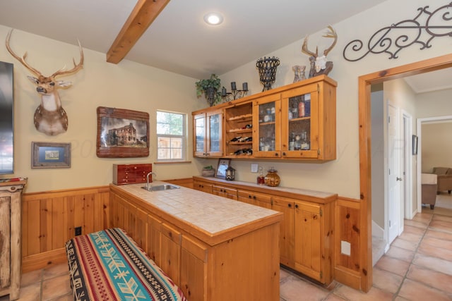 2314 Atkinsen St, Amarillo, TX 79106 - kitchen featuring tile countertops, a peninsula, wainscoting, wooden walls, and beam ceiling