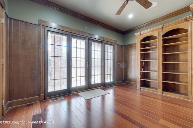 spare room with wood walls, french doors, ceiling fan, ornamental molding, and dark hardwood / wood-style flooring