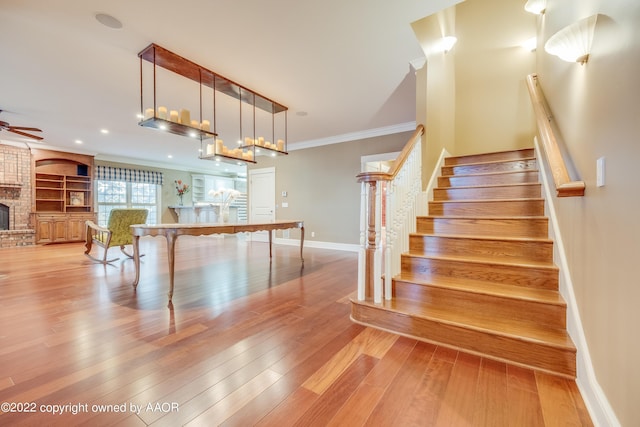 stairway with built in shelves, wood-type flooring, ornamental molding, and a brick fireplace