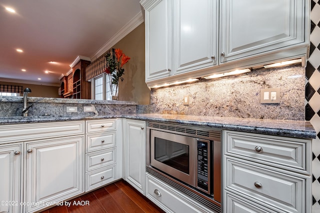 kitchen with stainless steel microwave, backsplash, dark stone countertops, ornamental molding, and kitchen peninsula