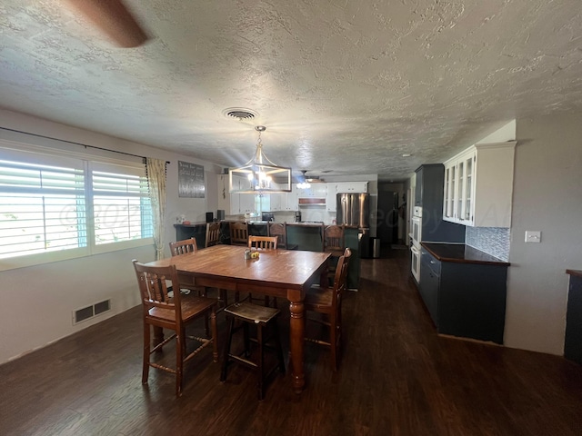 dining space featuring dark wood-type flooring, ceiling fan with notable chandelier, and a textured ceiling