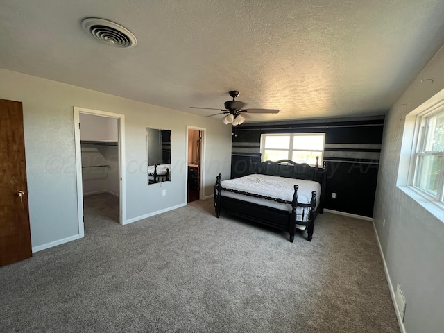 carpeted bedroom with multiple windows, ceiling fan, a walk in closet, and a textured ceiling