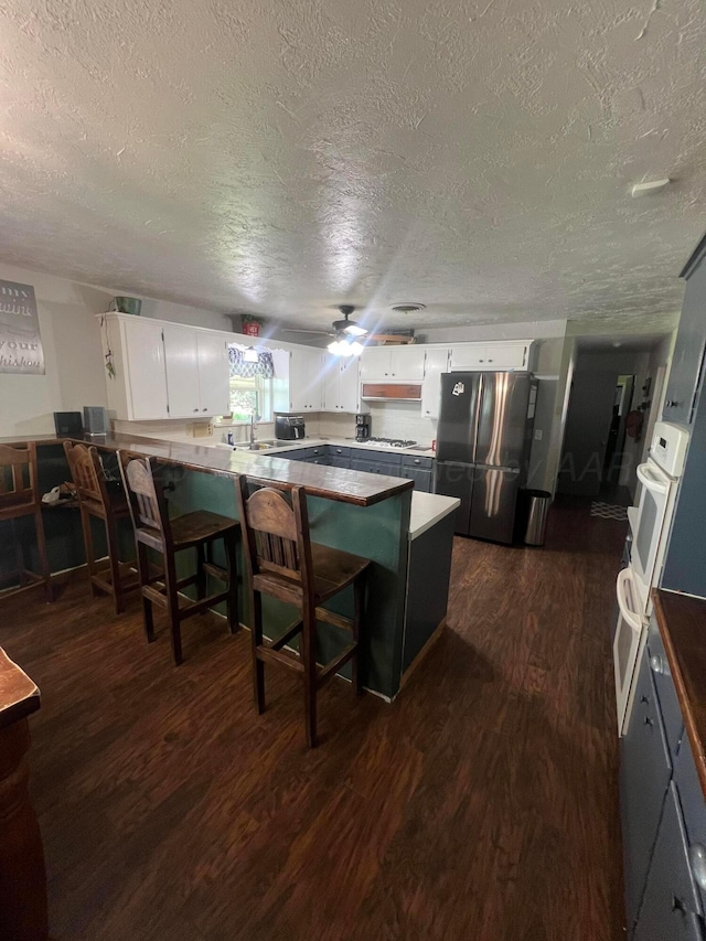 kitchen featuring a breakfast bar area, stainless steel refrigerator, white cabinetry, dark hardwood / wood-style floors, and kitchen peninsula