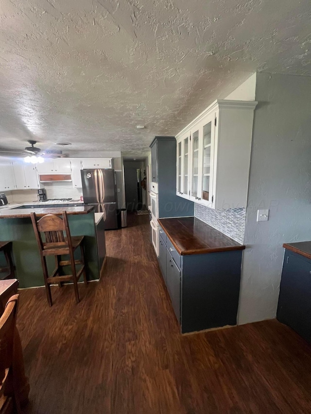 kitchen with a breakfast bar area, stainless steel refrigerator, dark hardwood / wood-style floors, kitchen peninsula, and white cabinets