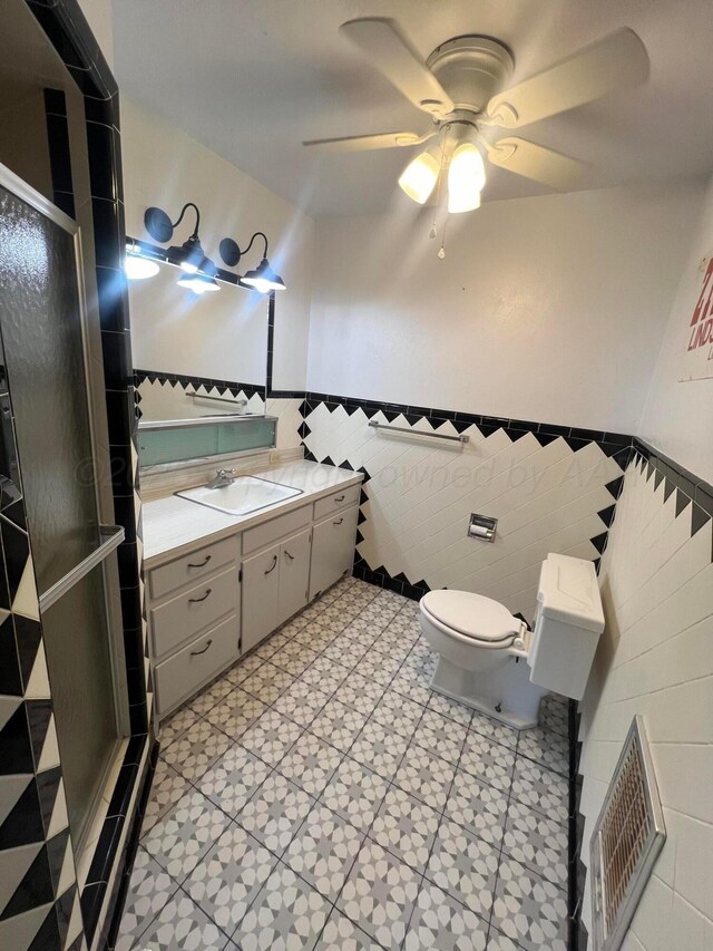 bathroom featuring tile walls, vanity, walk in shower, ceiling fan, and toilet