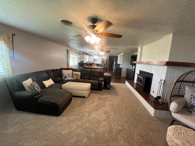 living room featuring ceiling fan, a fireplace, carpet, and a textured ceiling