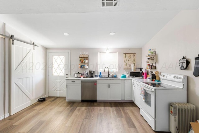 kitchen featuring appliances with stainless steel finishes, sink, a barn door, white cabinets, and radiator heating unit